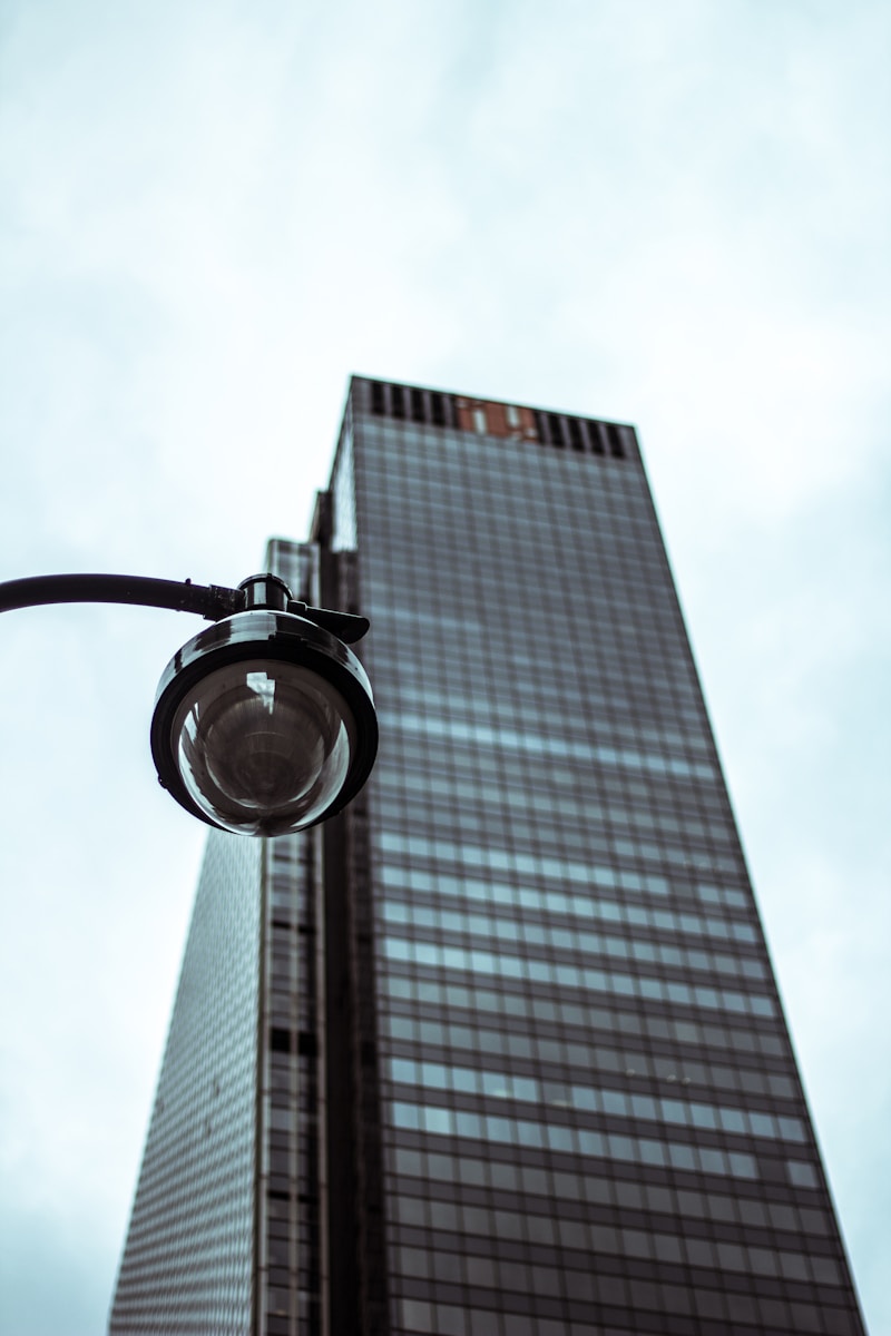 Street lamp positioned low, illuminating a modern high-rise building against a cloudy sky, highlighting urban architecture and ambiance.