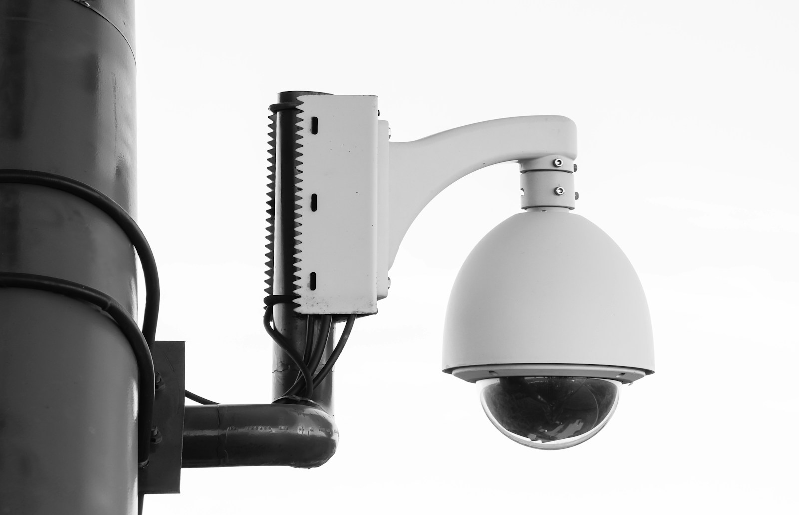 Surveillance camera mounted on a pole, showcasing its round lens and secure fittings, highlighting urban security measures.